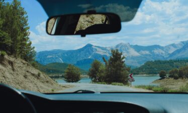 View from car interior of a winding road and mountain range with lush scenery, ideal for travel inspiration.