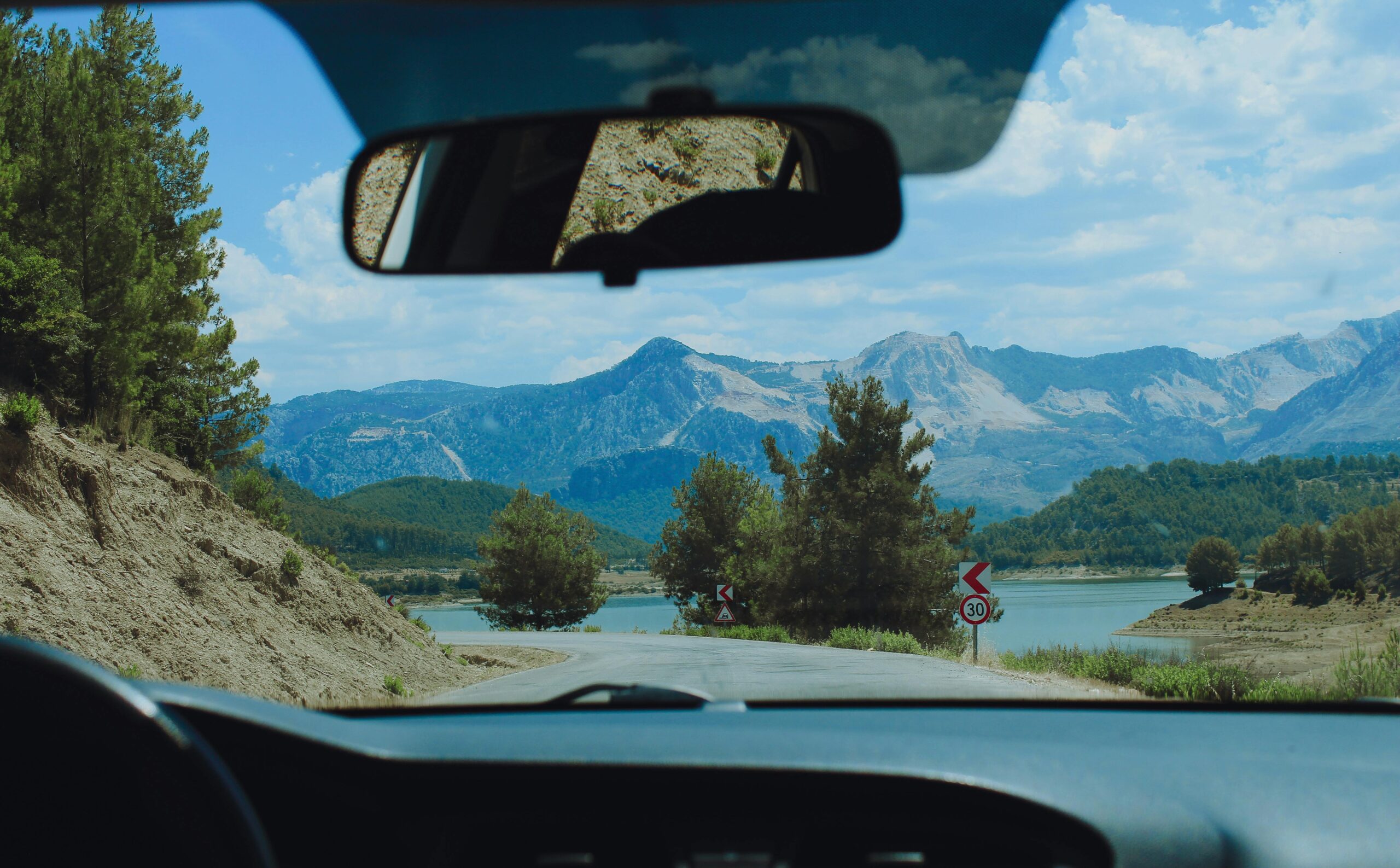 View from car interior of a winding road and mountain range with lush scenery, ideal for travel inspiration.