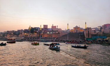 Boats on the Ganges River with Varanasi Ghats at sunset, showcasing Indian cultural heritage.
