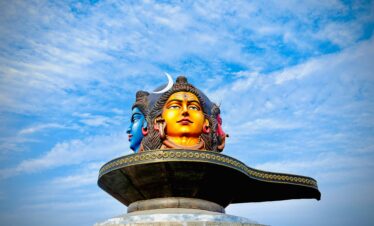 Vibrant three-headed Shiva statue under a blue sky in Pokhara, Nepal.